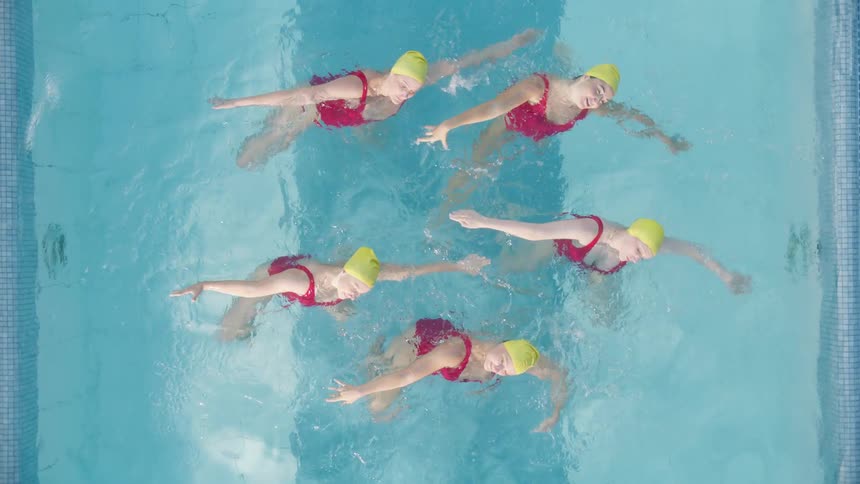 Five women swim in sync in an outdoor swimming pool