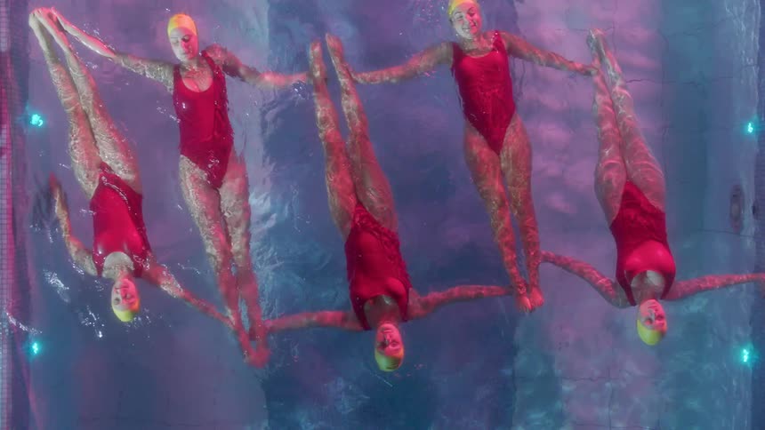 Women in red swimsuits perform synchronized swimming in a pool