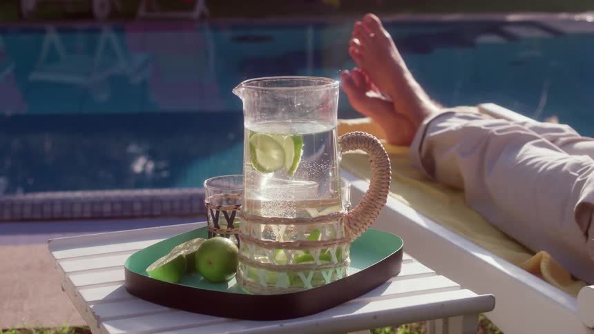 A pitcher of drink sits on a tray on a table next to an outdoor pool