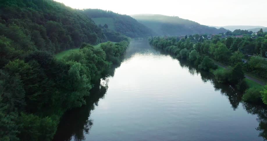 A river runs by hills and trees next to a road and a small town