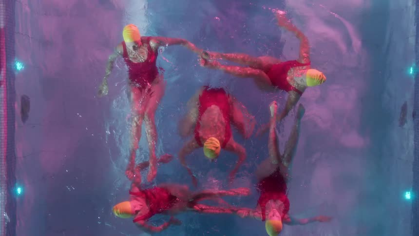 Five women synchronize swim in an outdoor swimming pool at night