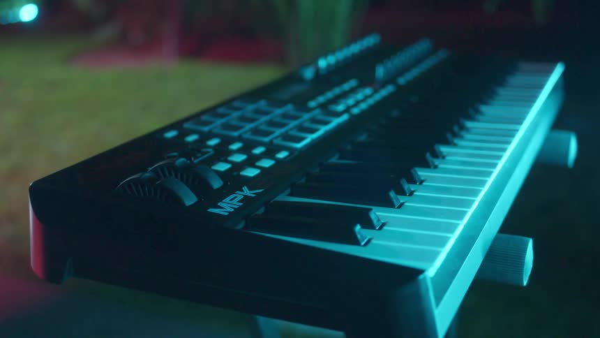 A musical keyboard with many knobs and buttons in a room with blue tinted light
