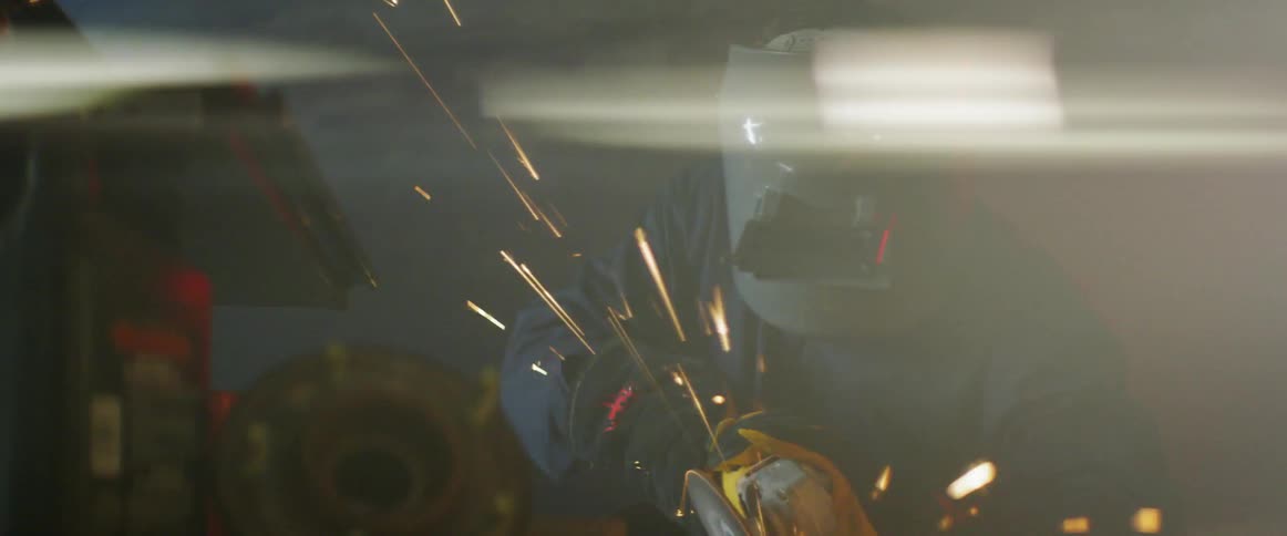 A person wearing protective gear uses a power saw to cut something metal