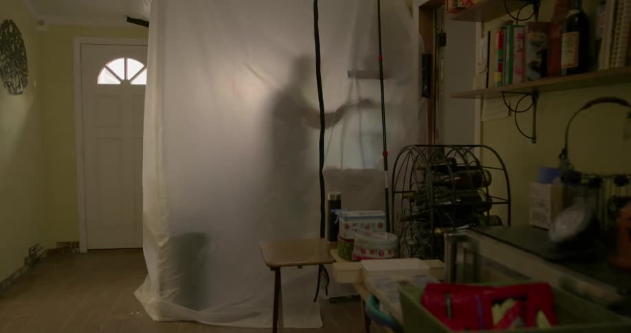 A man stands inside plastic sheets while painting a wall