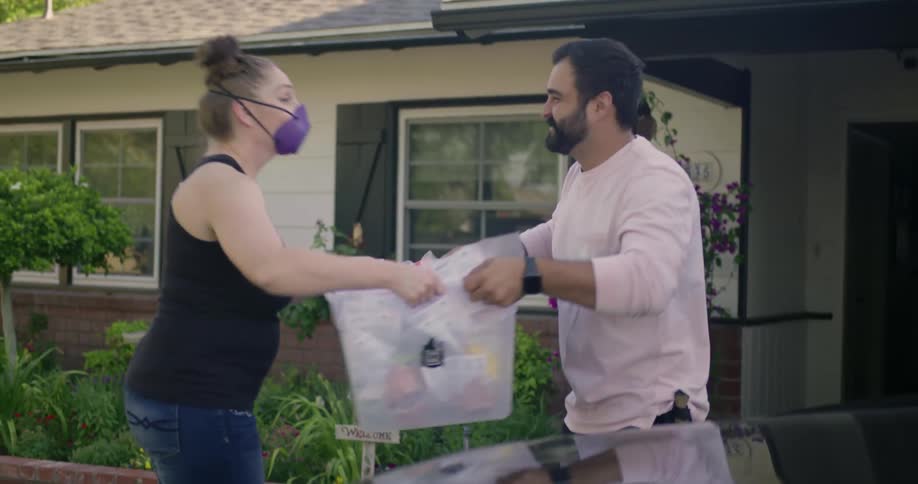 A man is bringing a basket of items out of a home to a woman who takes the basket away