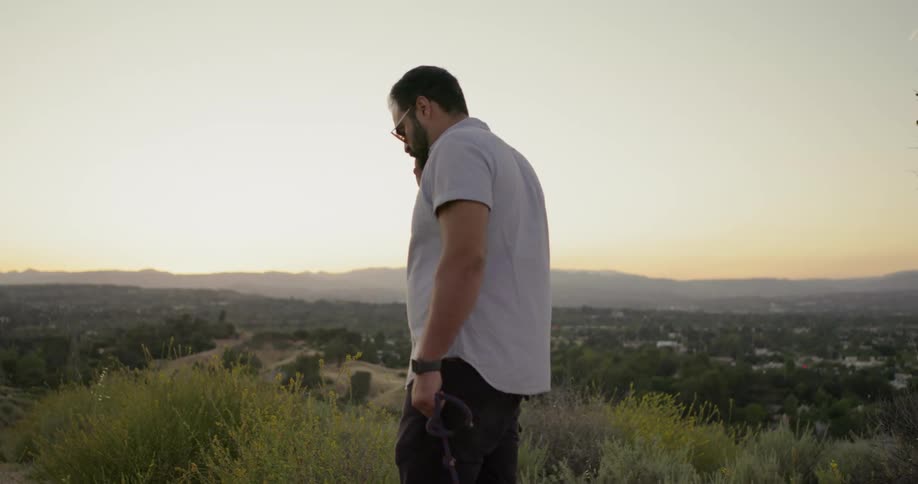 A man standing on a hill overlooking a town listening to his phone