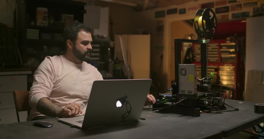 Man works with 3d printer and laptop in workshop
