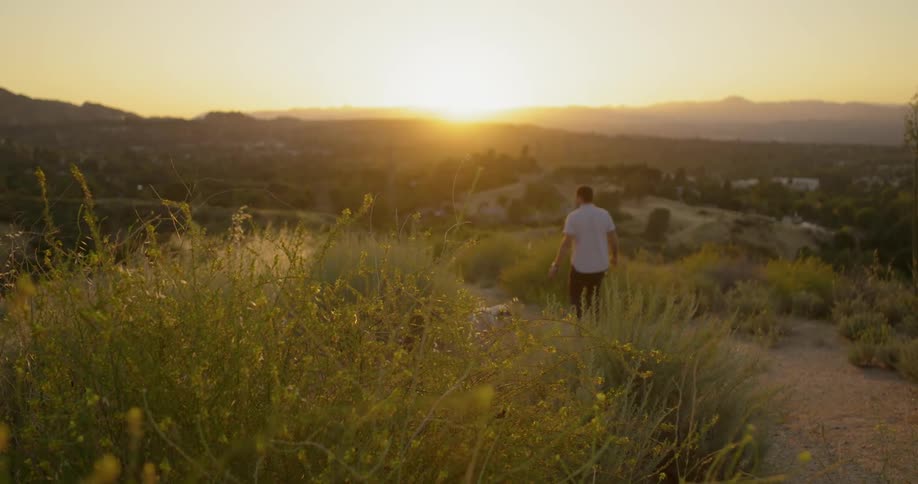 Man walks down a dirt path on the hills at sunset
