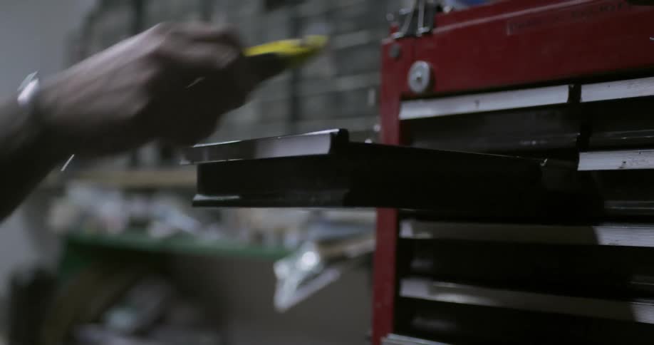 A white man opens a tool chest drawer and removes a utility knife