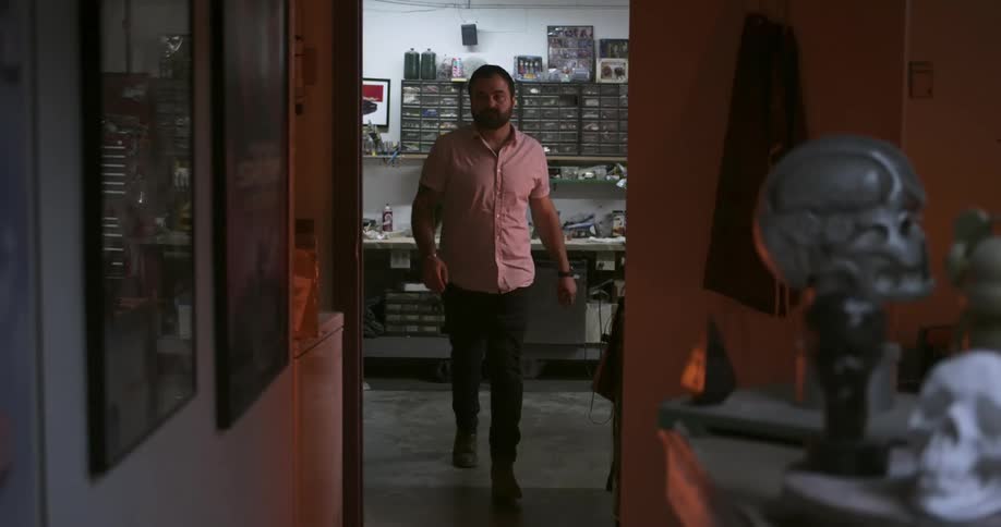 A white male walks out of a workshop area and goes through a doorway