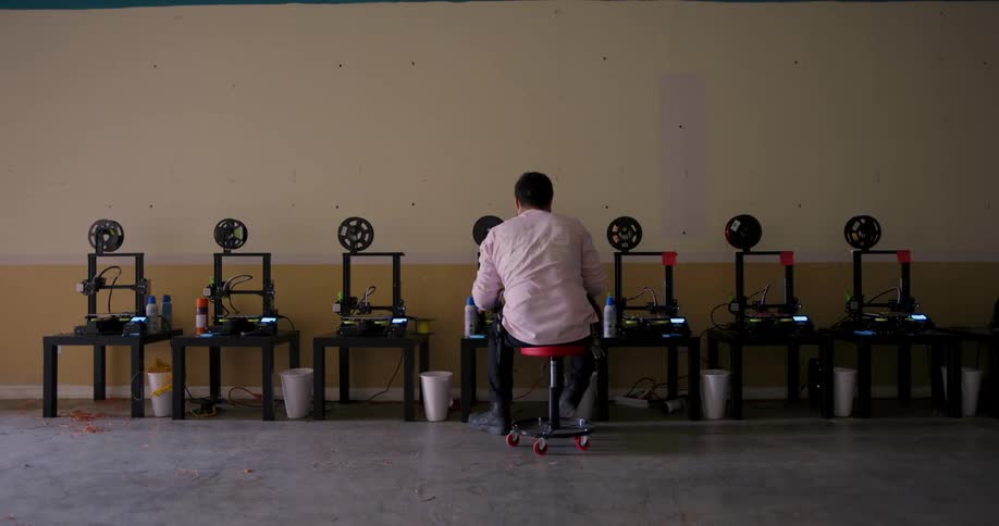 A white man on a stool rolls down a row of machines checking each one