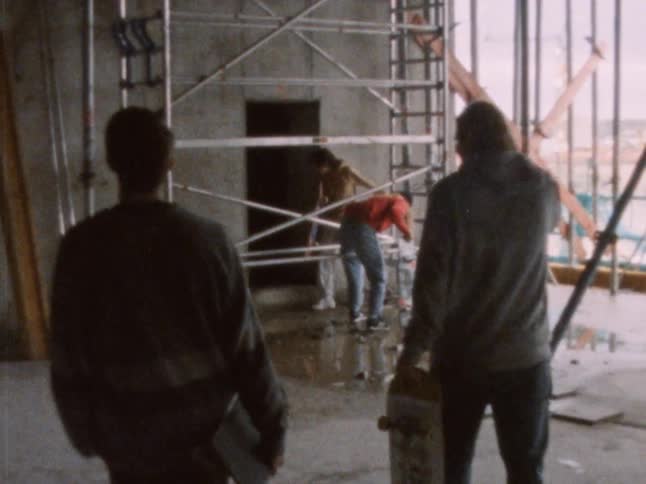 Four teens carrying skateboards climber over scaffolding on a construction site