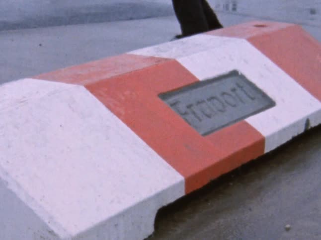 A man skateboards over an orange and white striped jump in the rain