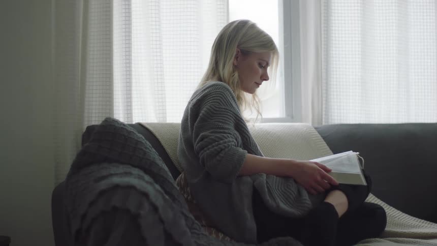 A young white woman sits on a couch reading a book