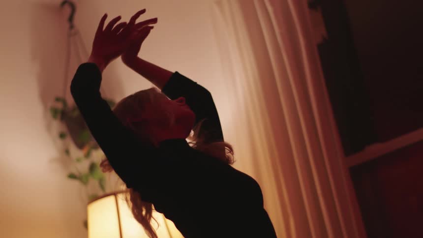 Woman with a black sweater dances slowly in the living room at home