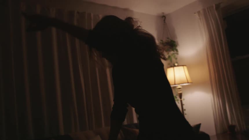 Woman withblack sweater and blonde hair dances slowly in the living room at home