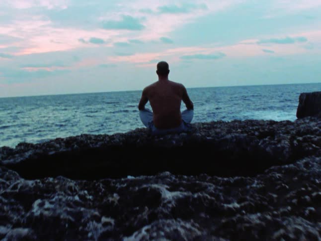 A man is sitting by the water on the rocks