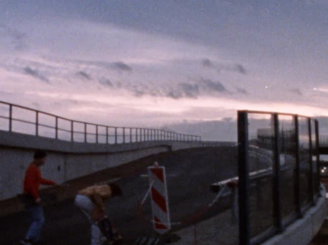 Four young white guys with skateboards walk up a concrete ramp