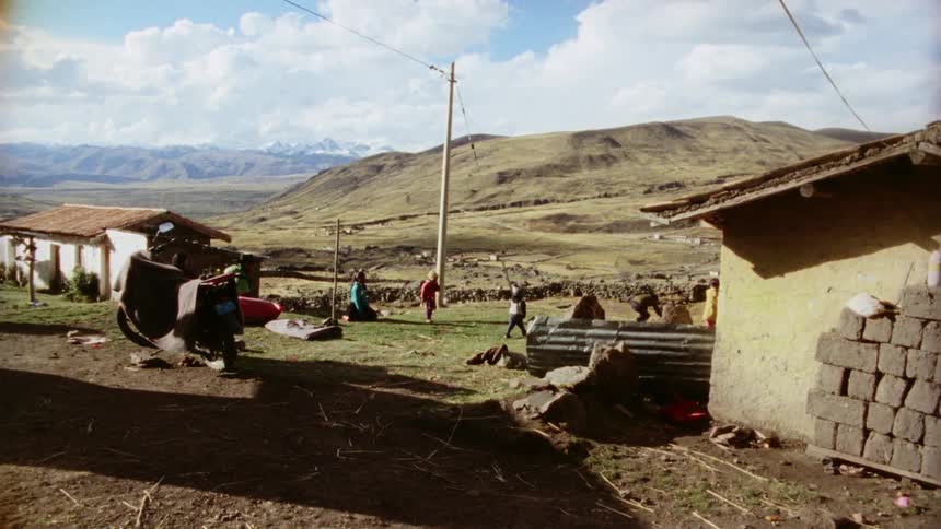 Children play with a soccer ball in the grass near small homes in a very rural area