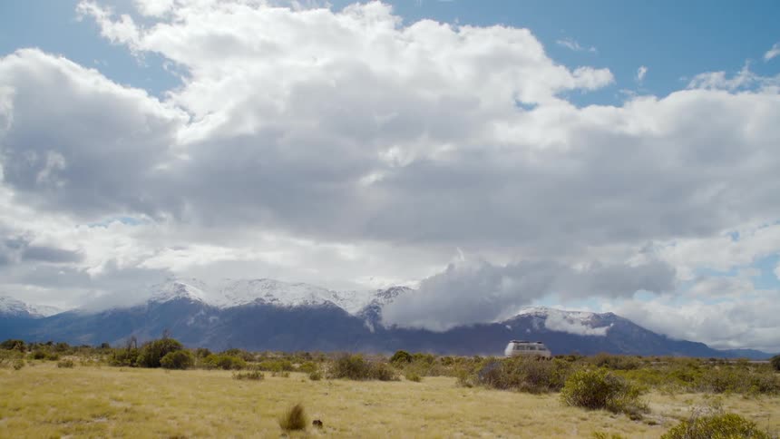 A medium sized van drives on a highway with snow capped mountains in the background