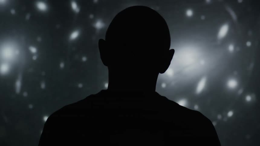 Man silhouetted in dark room looks up to projected image composed of lights and shadows