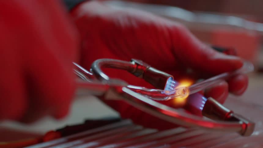 A man uses a a tool with heat to cut glass