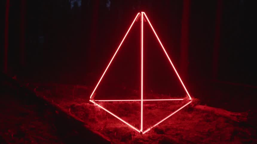 A fixture of red lights in a pyramid formation illuminating a dark woodland at night