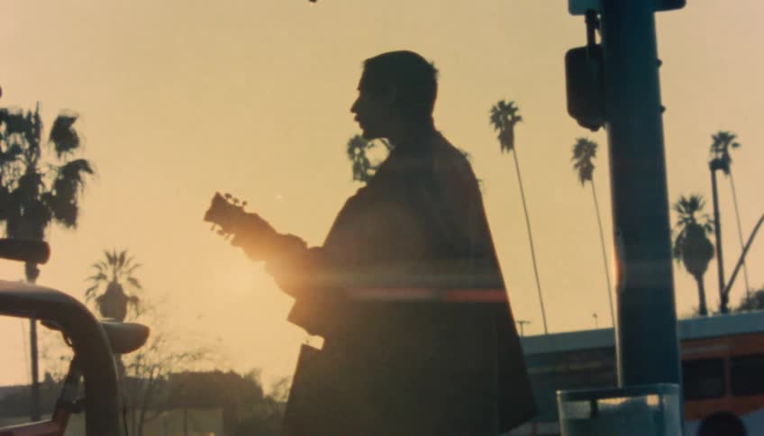 A woman gives money to a man playing a guitar on a street corner
