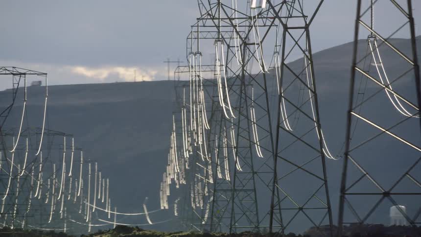 Very dynamic shot of high energy Hydro electric power lines on transmission towers in the desert near mountains