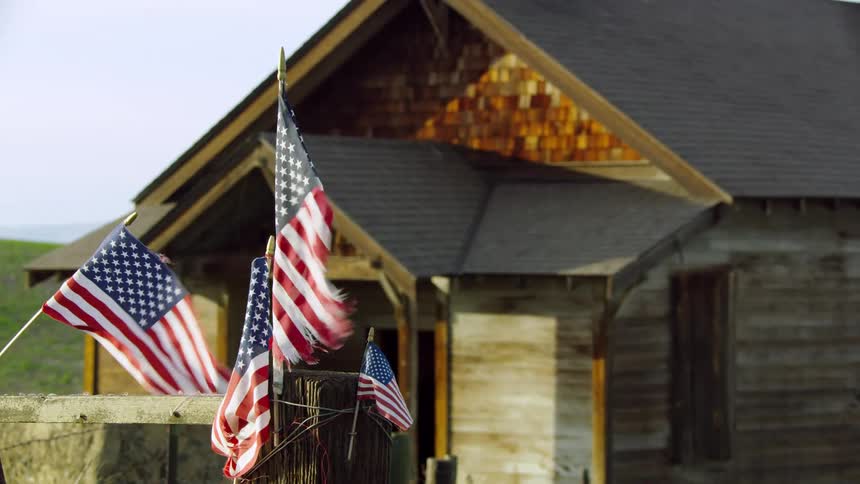 Several American flags flutter in the wind outside of a house in a rural area deep in the heartland of America