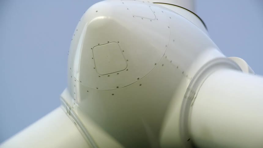 Tight shot looking up at the hub of the rotating wind turbine power generating windmill as it creates clean renewable energy and electricity