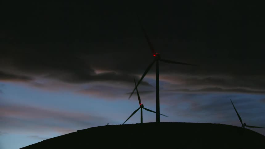 Blue hour low altitude aerial shot of wind turbines silhouetted against a moody sky in this pleasing and dynamic shot