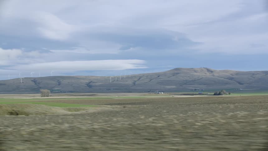 Passenger in a ranch truck point of view looking at the window at a ridge withe tan meadow grass and fields of early spring growth in the foreground