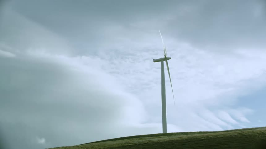The camera looks up at a lone windmill and dynamic weather clouds as the wind farm creates renewable clean electricity for electric grid households and businesses