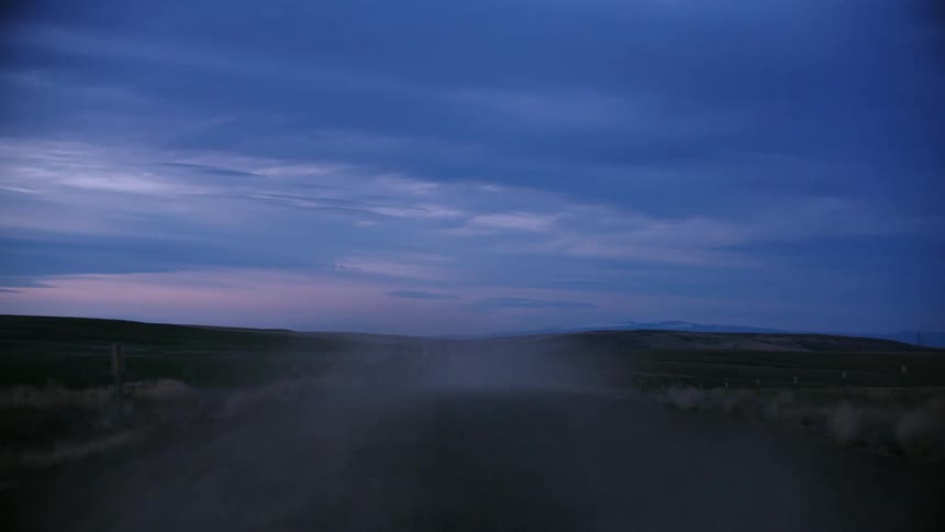 Blue hour dusk driving on rural dirt road as dust flies high into the late evening sky in rural America
