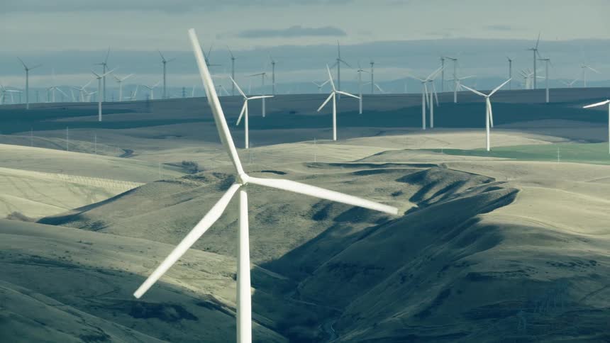 The camera rotates around one turning windmill as many more are seen in the background all turning and generating large amounts of green renewable clean electricity