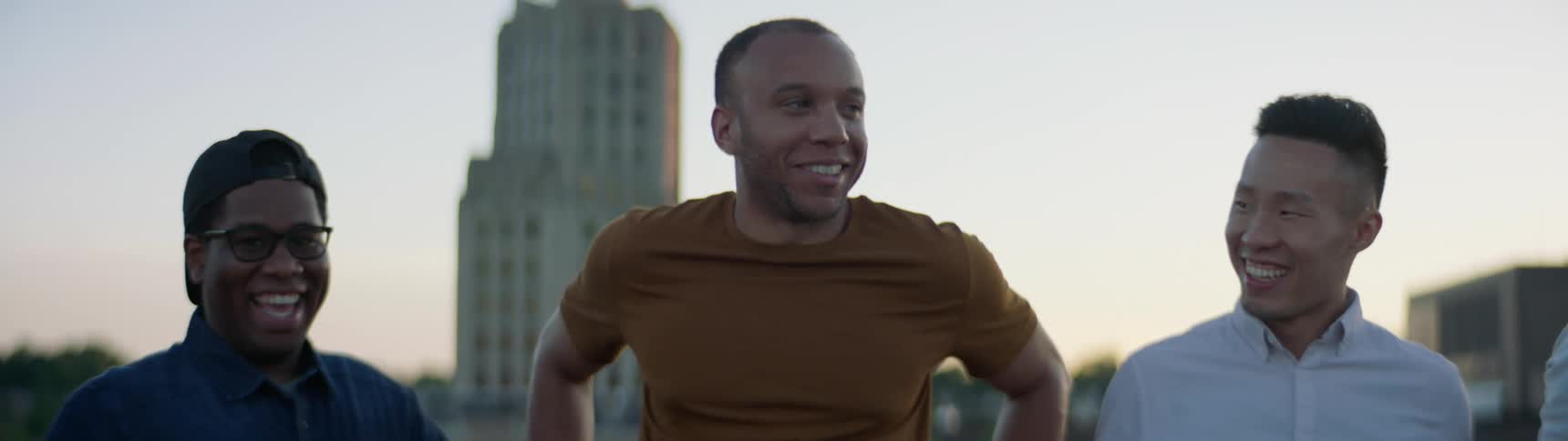 Two black men and an asian man smile and talk while standing in a park