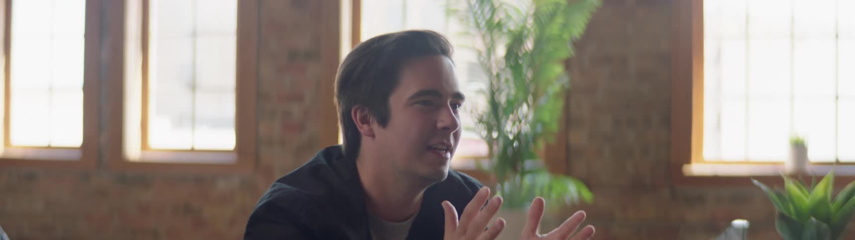 A young white man sits in a room and talks animatedly with others