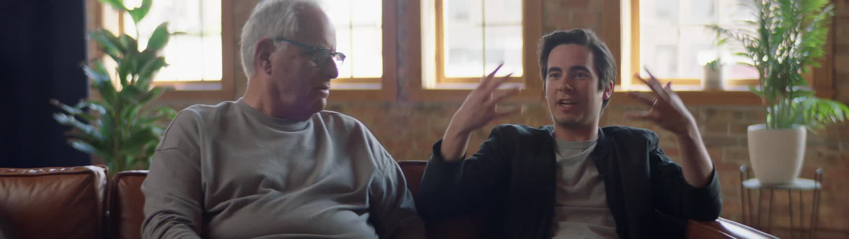 A young man sits on a couch and talks with his grandfather