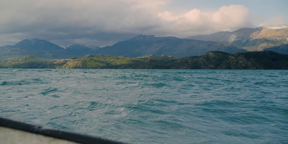 Boat sails across the blue sea with mountains and clouds in the background