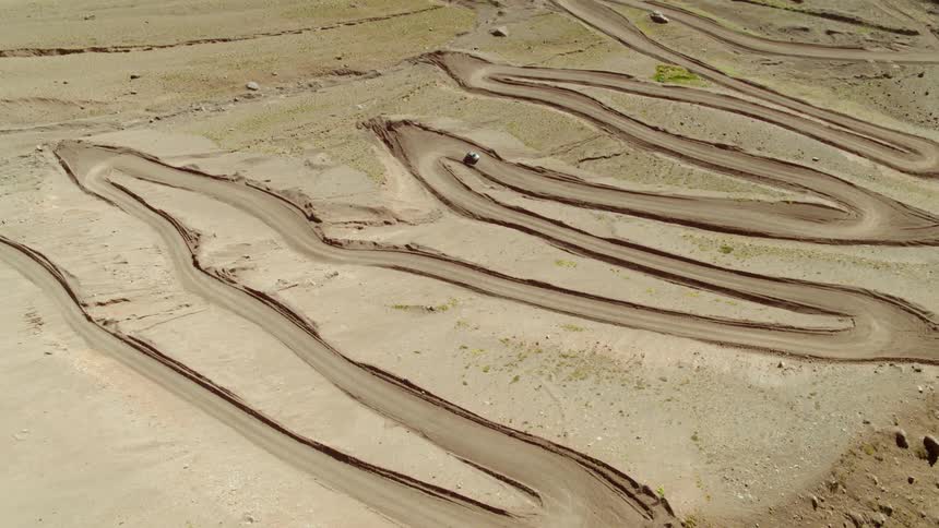A car is driving on a winding trail in the desert
