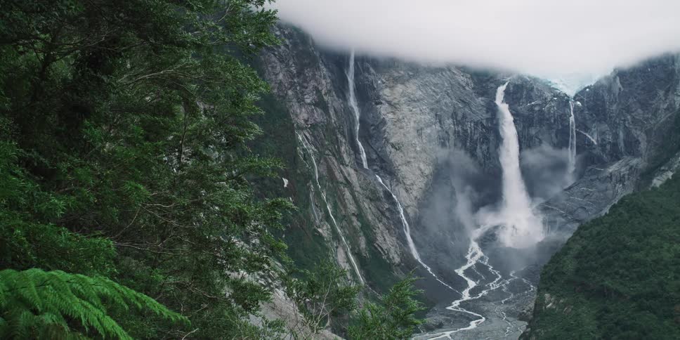 White water rushes and flows down the face of cliffs into a ravine on a cloudy foggy day