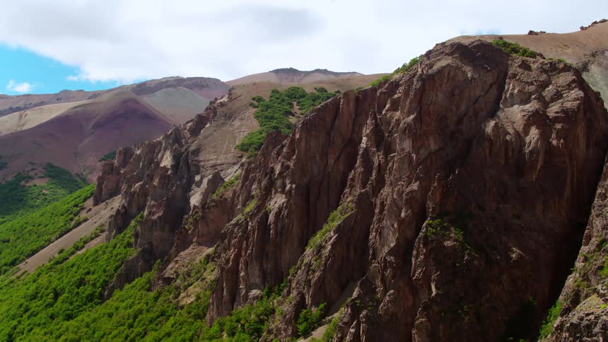 Lush green trees and bushes grow densely below a canyon