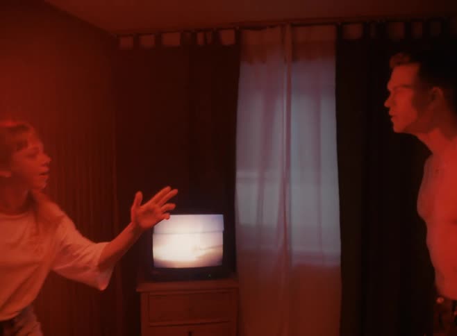 Shirtless man and blonde woman in the red light argue furiously in a room