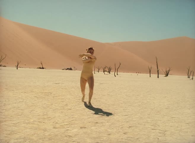 A ballet dancer performs ballet in the desert with dead trees in the background