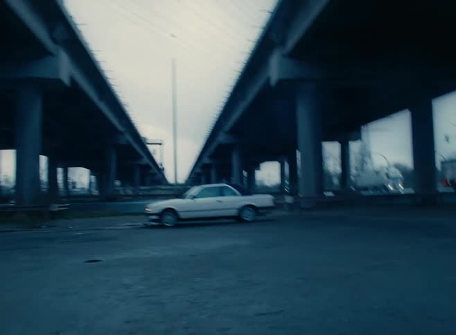 A small car coming to a stop underneath a pair of bridges