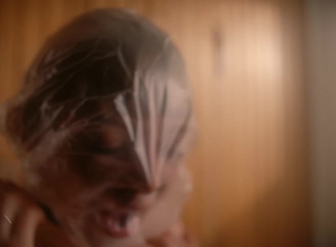 A woman pulls a plastic bag tighter over her head and struggles to breathe