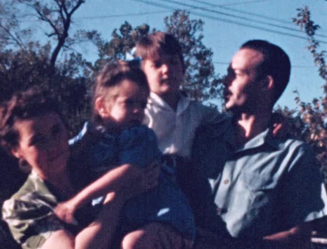 A mother and father carrying their daughter and son standing together as if to pose for a photograph