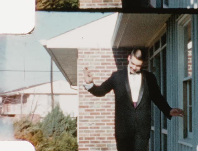 A teenager waves as he walks out of his house wearing a tuxedo