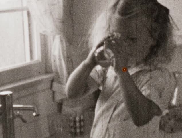 A young cleans a glass in the sink then drinks from it as her sister watches
